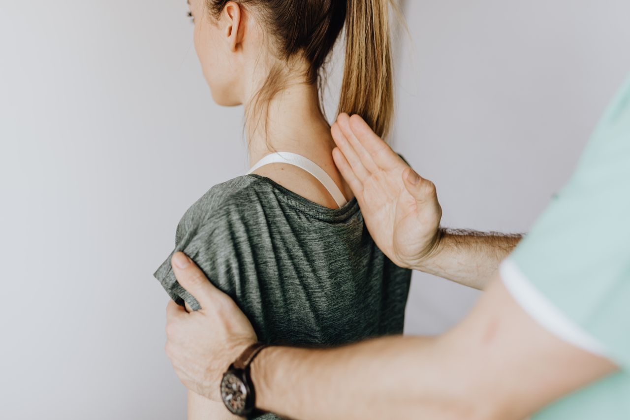 contact-img Back view of crop unrecognizable osteopath in uniform and wristwatch checking up back of slim female patient in casual wear on white background